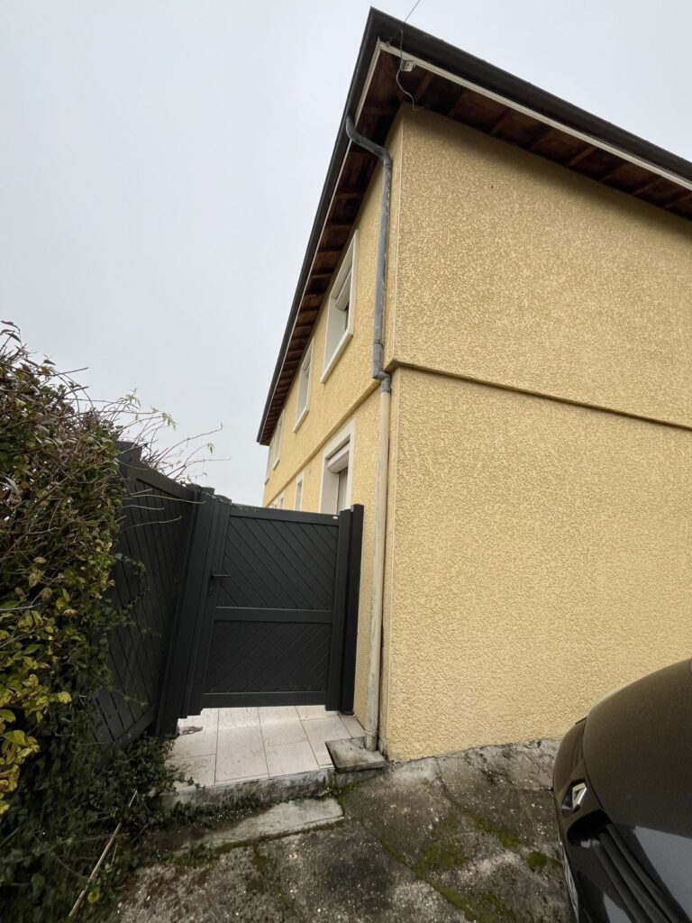 Façade latérale d'une maison crépie jaune avec portail gris, à Lyon