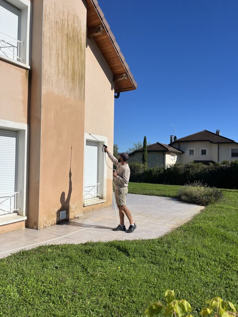 Artisan nettoyant à la lance une façade enduite marquée de traces vertes, à Lyon